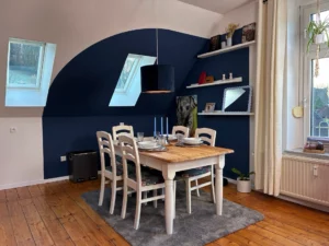 Ferienwohnung Remscheid – Wohnzimmer Sitzbereich Übersicht Wohnzimmer mit rotem Sessel, grauem Sofa und Hängeleuchten in der Ferienwohnung Remscheid