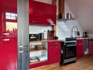 Ferienwohnung Remscheid – Wohnzimmer Sitzbereich Übersicht Wohnzimmer mit rotem Sessel, grauem Sofa und Hängeleuchten in der Ferienwohnung Remscheid